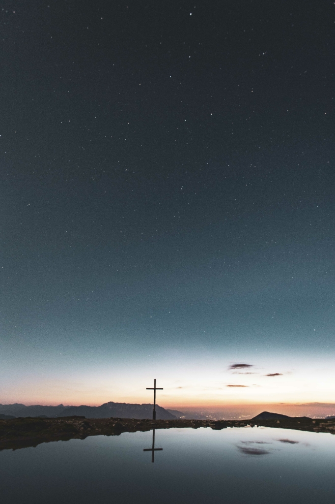 Sonnenuntergang und Sternenhimmel am Gipfel beim Gipfelkreuz des Trattberges mit kleinem Gebirgssee, Tennengau, Salzburg, Österreich.