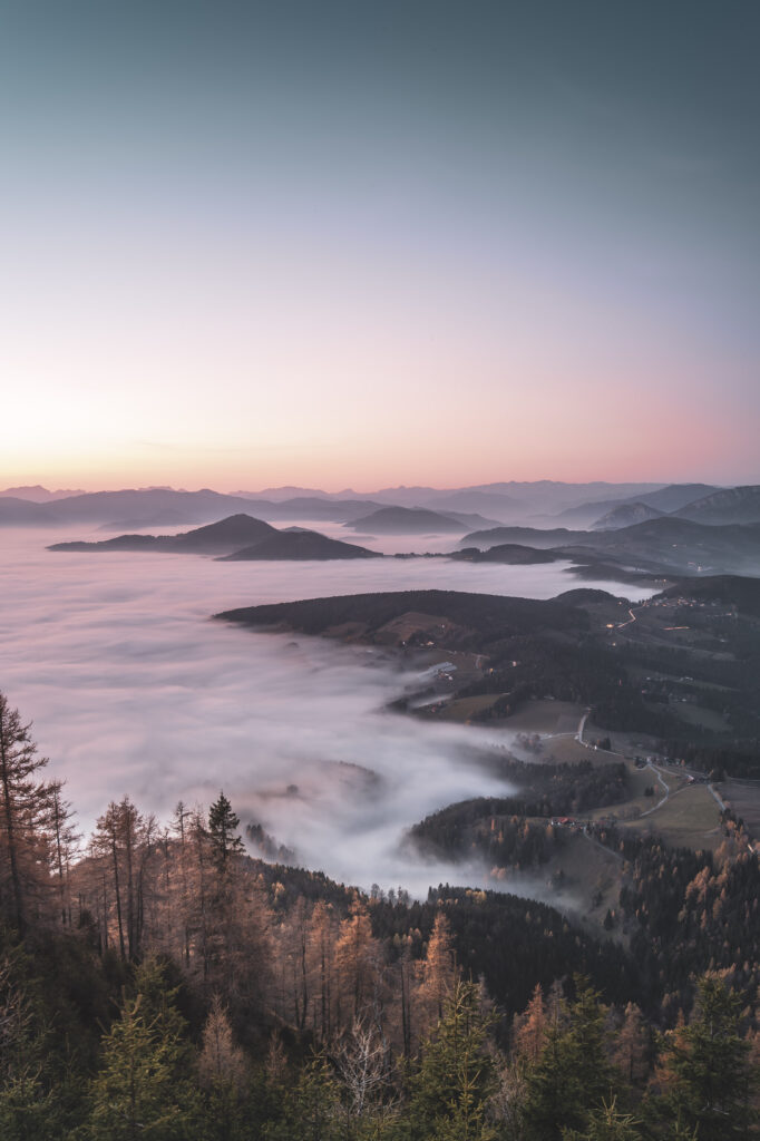 Nebeldecke über dem Grazer Bergland. Sonneuntergang am Gipfel des Grazer Hausberges Schöckl im Herbst, in der Steiermark, Österreich.