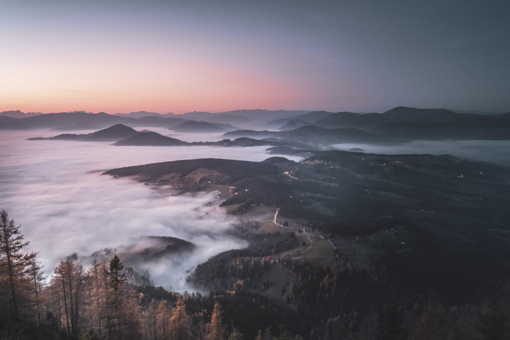 Nebeldecke über dem Grazer Bergland. Sonneuntergang am Gipfel des Grazer Hausberges Schöckl im Herbst, in der Steiermark, Österreich.
