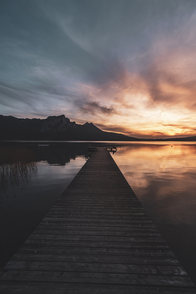 Am Steg beim Badeplatz Loibichl am Mondsee mit Sonnenuntergang und Drachenwand im Hintergrund an der Grenze von Salzburg und Oberösterreich, Österreich.
