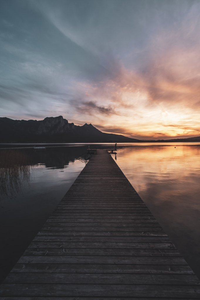 Am Steg beim Badeplatz Loibichl am Mondsee mit Sonnenuntergang und Drachenwand im Hintergrund an der Grenze von Salzburg und Oberösterreich, Österreich.