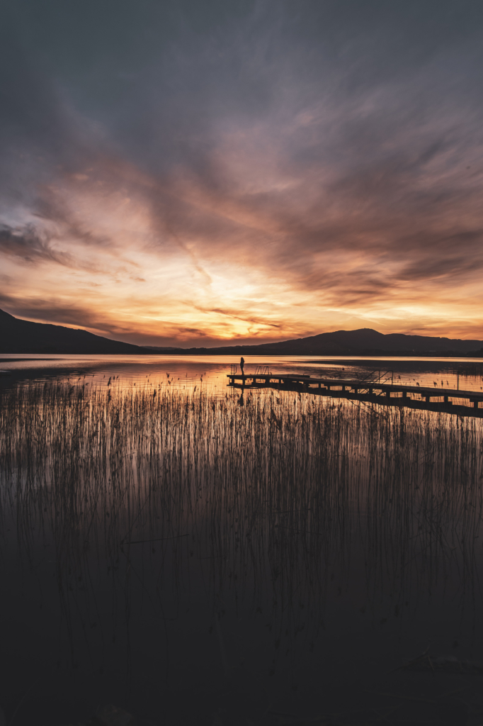 Am Steg beim Badeplatz Loibichl am Mondsee mit Sonnenuntergang und Drachenwand im Hintergrund an der Grenze von Salzburg und Oberösterreich, Österreich.