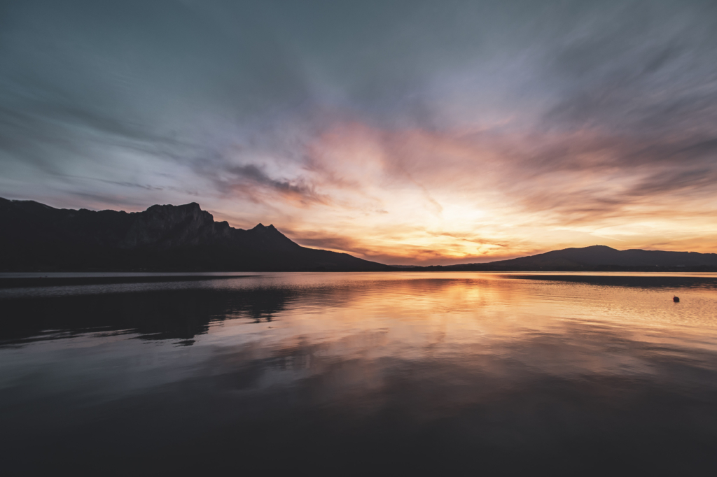Am Steg beim Badeplatz Loibichl am Mondsee mit Sonnenuntergang und Drachenwand im Hintergrund an der Grenze von Salzburg und Oberösterreich, Österreich.
