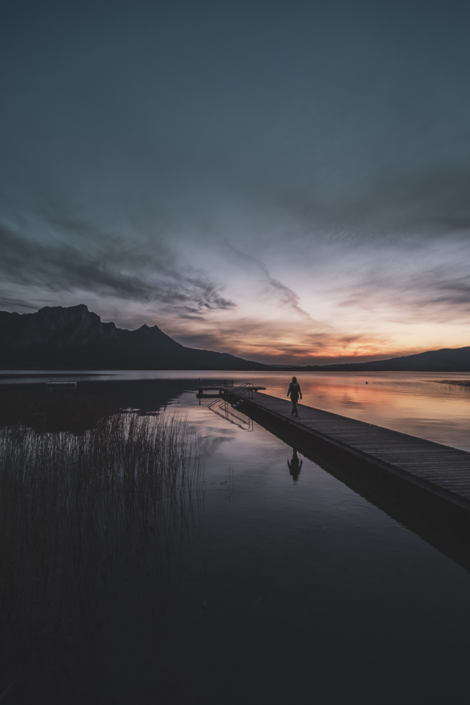 Am Steg beim Badeplatz Loibichl am Mondsee mit Sonnenuntergang und Drachenwand im Hintergrund an der Grenze von Salzburg und Oberösterreich, Österreich.