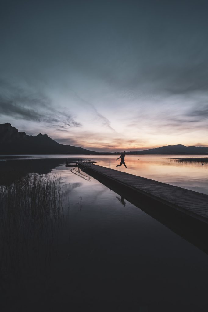 Am Steg beim Badeplatz Loibichl am Mondsee mit Sonnenuntergang und Drachenwand im Hintergrund an der Grenze von Salzburg und Oberösterreich, Österreich.