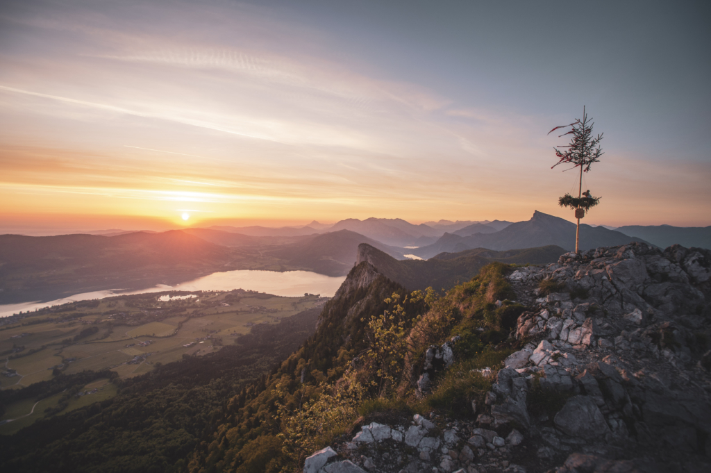 Frühlingshafter Sonnenaufgang mit Blick auf die Drachenwand und Mondsee am Schober mit Maibaum in den Salzkammergut-Bergen an der Grenze von Oberösterreich und Salzburg, Österreich.