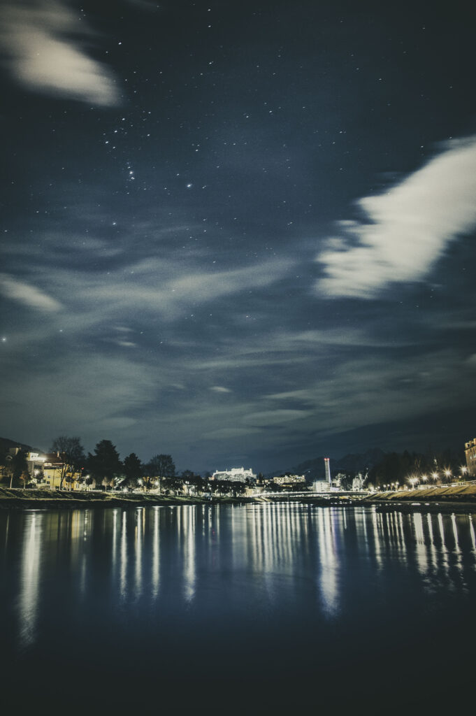 Blick über die Salzach und die Stadt Salzburg bei Nacht mit der Festung Hohensalzburg im Hintergrund in Österreich.