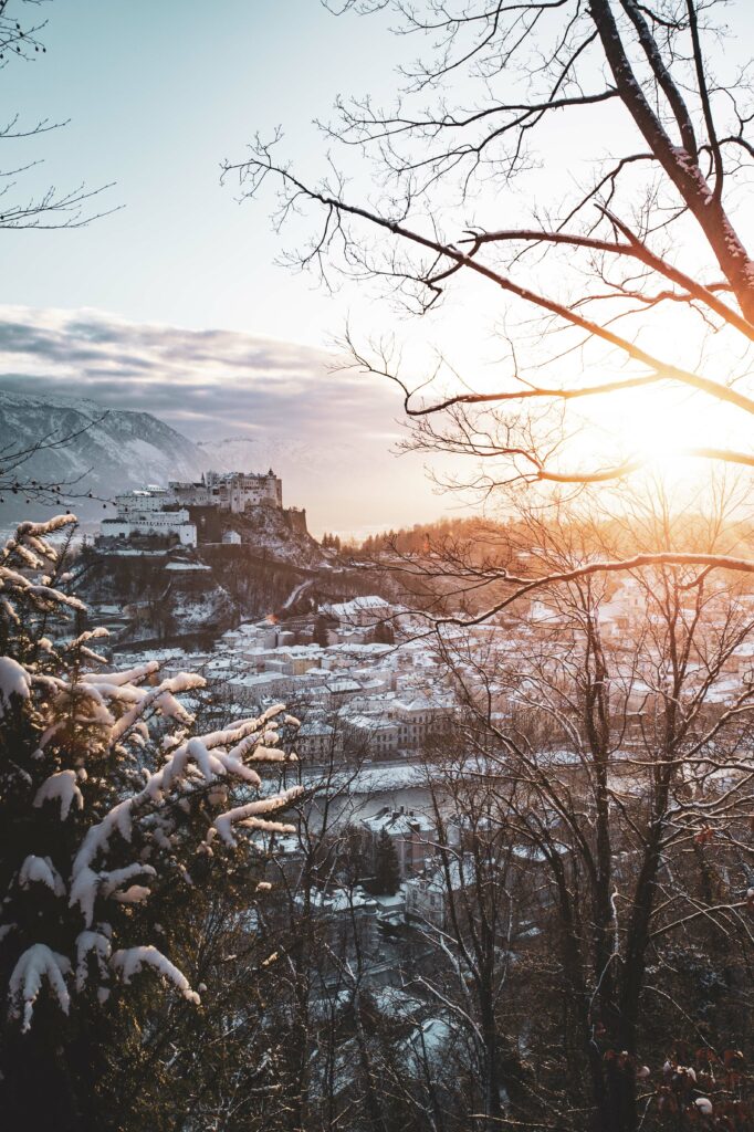 Blick vom Kapuzinerberg auf die verschneite Stadt Salzburg und die Festung Hohensalzburg während eines Sonnenuntergang im Winter.