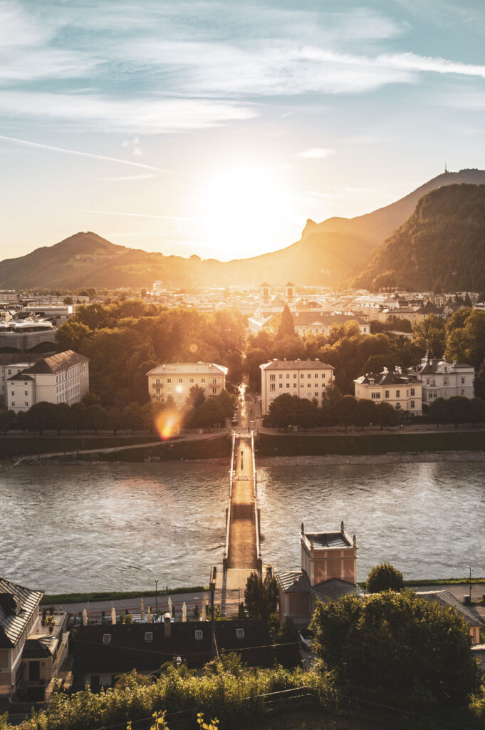 Sommer Sonnenaufgang am Salzburger Mönchsberg, der Mozartstadt an der Salzach. Die Sonne am Horizont zwischen Heuberg, Nockstein und Gaisberg und die ersten Sonnenstrahlen am Müllner Steg.