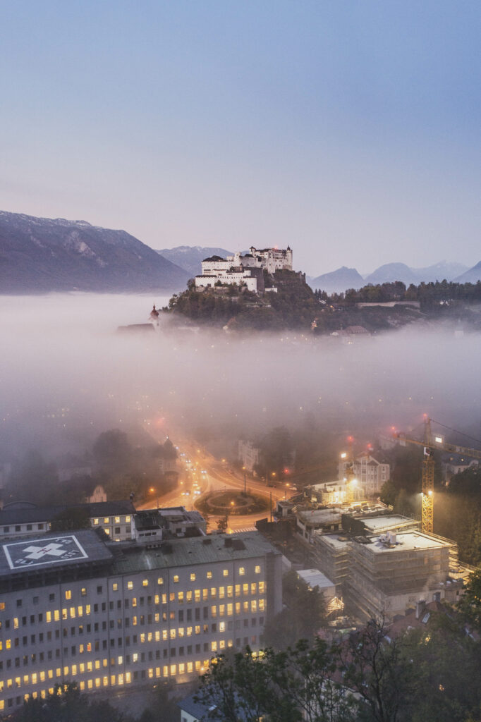 Festung Hohensalzburg am Mönchsberg ragt aus dem Morgennebel kurz vor Sonnenaufgang in der Mozartstadt Salzburg in Österreich.