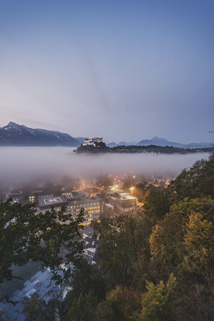 Festung Hohensalzburg am Mönchsberg ragt aus dem Morgennebel kurz vor Sonnenaufgang in der Mozartstadt Salzburg in Österreich.