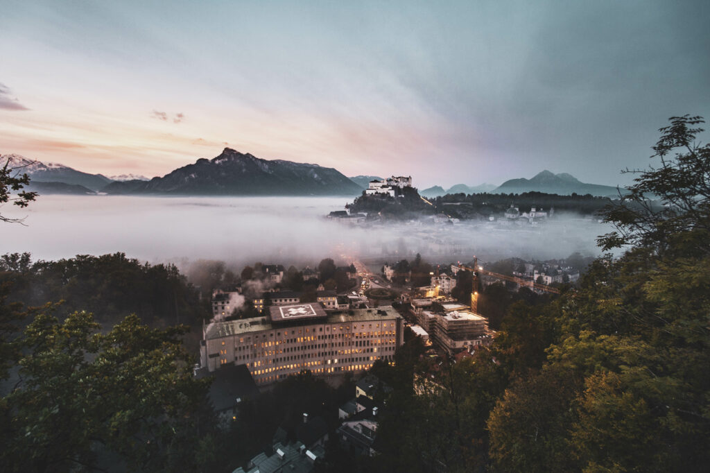 Festung Hohensalzburg am Mönchsberg ragt aus dem Morgennebel kurz vor Sonnenaufgang in der Mozartstadt Salzburg in Österreich.