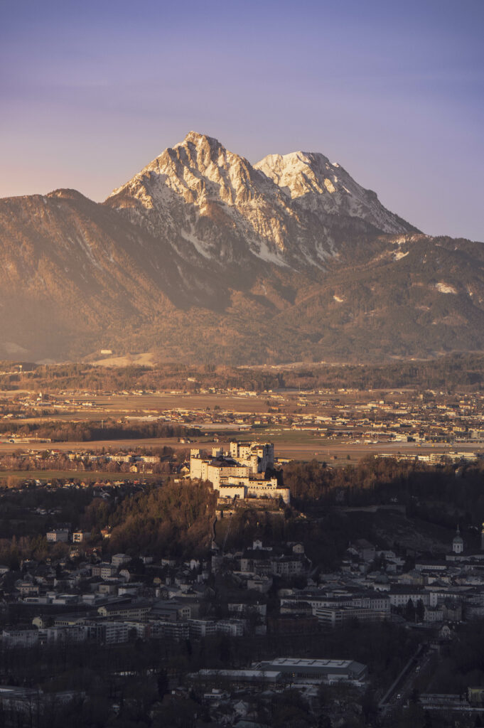 Sonnenaufgang über Stadt Salzburg mit Festung Hohensalzburg und Salzburger Dom. Bayrische Alpen mit dem Hochstaufen im Hintergrund.